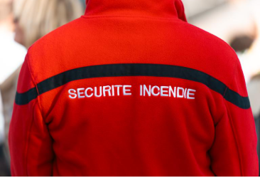A security agent in uniform checking a fire extinguisher and an emergency exit, the agent's back is to the camera.